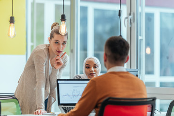 Obraz premium Group of coworkers, teammates helping their new African American, black, muslim colleague wearing hijab to integrate into the modern company. Multiethnic colleagues in a modern startup company.