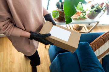 Young blonde girl in protective gloves holding cardboard boxes. Epidemic. Coronavirus. Covid-19. Quarantine. Shipping parcel during coronavirus time. Opening a package during a pandemic in home.