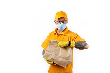 Cautious young man from a courier delivery service in a medical mask and gloves holds a package with an order in his hands and looks at his watch on a white background
