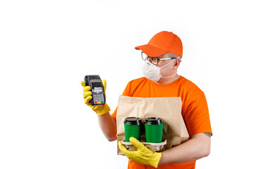 Cautious young man from a courier delivery service in a medical mask and gloves holds a cup of coffee in his hands, a package with an order and a terminal for cashless payment on a white background