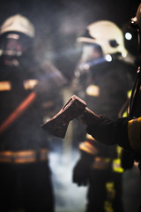 Group of professional firefighters wearing full equipment, oxygen masks, and emergency rescue tools, circular hydraulic and gas saw, axe, and sledge hammer. smoke and fire trucks in the background.