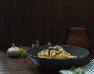 Homemade pasta with wild mushrooms in a gray plate on a dark wooden background, with space