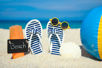 Beach summer holiday banner background. Flip-flops and hat with a board and ball on the sand near the ocean. Summer accessories on the seashore. Tropical vacation and relax travel concept.