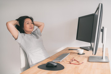 Working at home Asian mature woman taking a break from small business remote work at computer desk thinking of early retirement or success of online e-commerce. Chinese middle aged lady in her 50s.