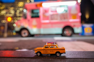 Yellow classic taxi model parked by the pink ice cream truck on a street in New York at dusk