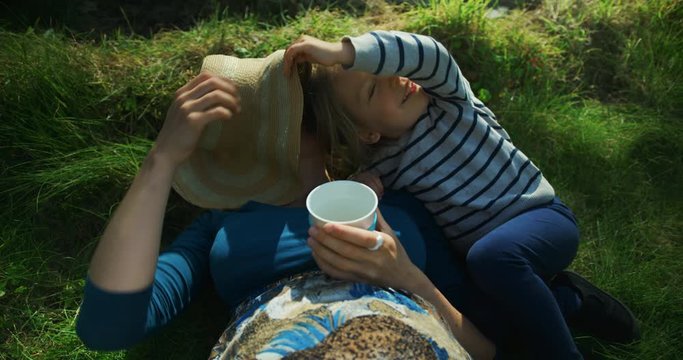 Preschooler in garden lifts his mother's hat to rest his head under it