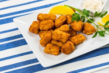 Crispy Fish Bites Snack Size. Deep Fried Pollock Fish Fingers with Tartar Dipping Sauce on a Wooden Board. Selective focus.