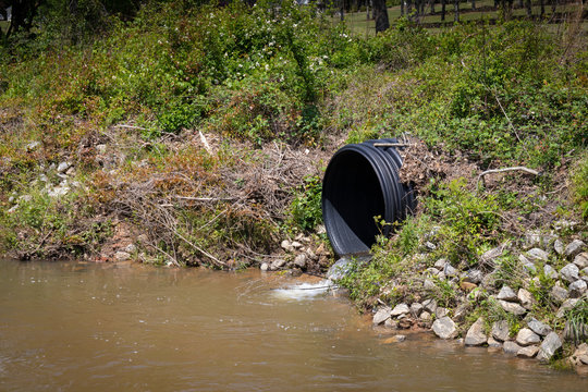 Black plastic drainage culvert pipe releasing water into a stream, environmental safety issue, horizontal aspect