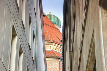 Worm's-eye view of narrow alley with subtle details of Frauenkirche cathedral, landmark building of Bavarian capital Munchen, at the end of street in downtown district Altstadt, Bayern Germany Europe