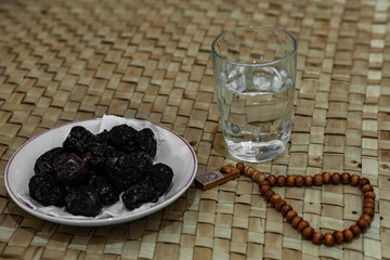 Ramadan food and drink in rural area or countryside concept. Muslim fasting. Dates fruits, prayer beads, drinking water on traditional mat.