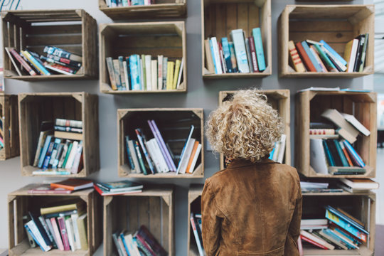 Rear View Of Woman Standing Against Book Shelves In Library