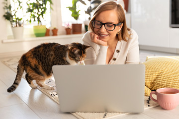 Woman freelancer lies on carpet in living room, watch webinar. Female with her cat talking through...