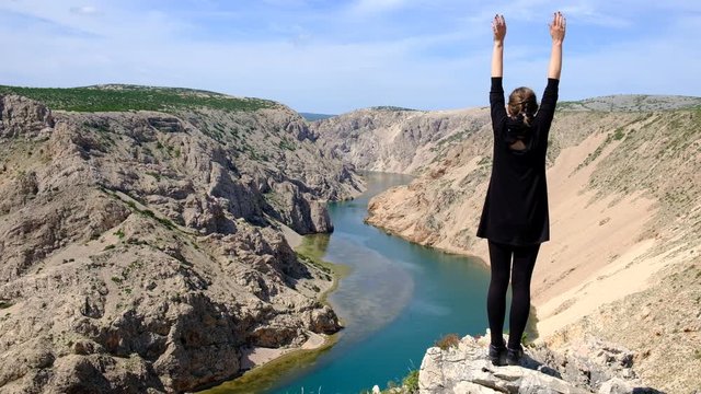 Girl in a black dress stretching and enjoying the breathtaking view of the Zrmanja canyon in Croatia. Sense of freedom travelling in Europe on the top of canyon overlooking still turquoise water.