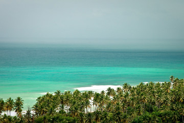 Beach landscape with sand, white foam waves, palm trees, blue sky, turquoise water and clouds, paradise Caribbean coast of Dominican republic 