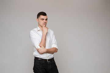 Waist up of handsome young man in white shirt holding hands in pockets while posing against black background