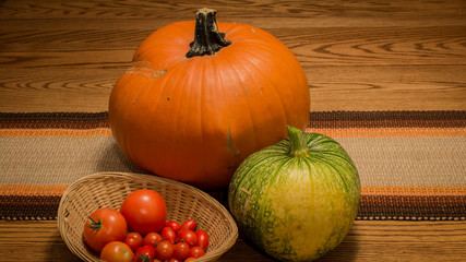 Pumpkins and Tomatoes Autumn Harvest Background. Wicker Basket with Red Tomatoes on a Wooden Table Decoration Display. Grown Food from a Farm for Thanksgiving Holiday