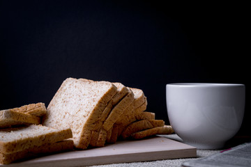 Homemade slide bread with hot coffee cup and newspaper on the wooden with copy space on black background