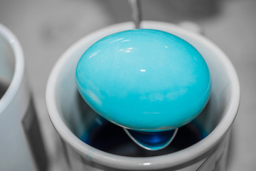 Dying Easter eggs tradition background. Blue bright Easter egg in a mug background. Blue colorful dye festive decoration