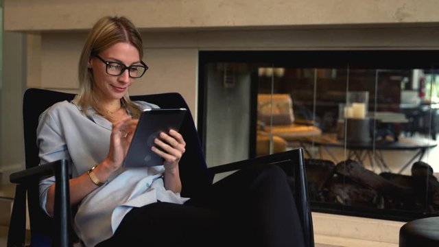 Millennial young woman with touch pad in hands sitting in comfortable chair and using free time for communication in social networks, Female internet user browsing web pager while shopping online
