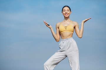 Beautiful girl standing on a sky background. Woman in a yellow top. Lady with phone in her hands