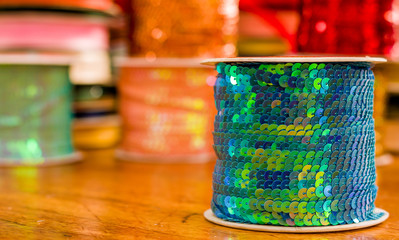 Cose up of shiny rolls of colorful sequins green tape, multi-colored over a wooden table in a blurred background