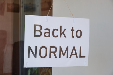 'Back to normal' sign hanging from a store window after Coronavirus (Covid-19) lockdown measures are being eased off. Economy restart concept.
