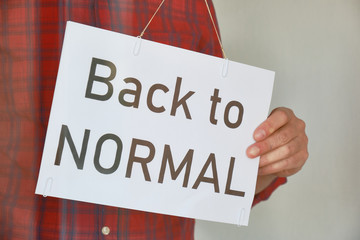 Economy restart after Coronavirus (Covid-19) concept. Shop or restaurant owner flips sign on window from 'Closed' to 'Back to normal' as countries are easing lockdown/isolation measures.