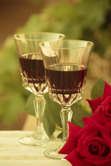 Two glasses of red wine next to some roses in a romantic setting