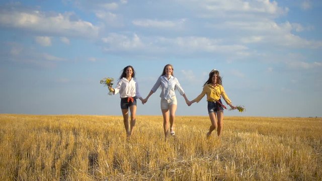 Three happy girls running on stubble field togerher, slow motion