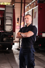Professional fireman portrait. Firefighter wearing uniform of shirt and trousers. Fire truck in the background.