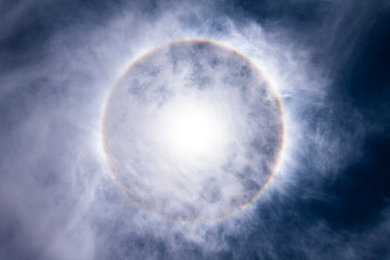 Obraz na płótnie Canvas The Sun, with an amazing halo around the sun created by light refraction because of ice crystals on the upper atmosphere layers in the troposphere that create this circumscribed circular sun halo 