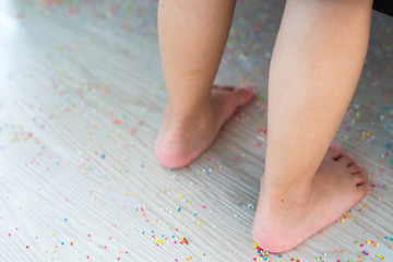 Colourful Sugar sprinkles, decoration on the wooden floor with a child foot stepping on. Messy and scattered. Childhood concept.