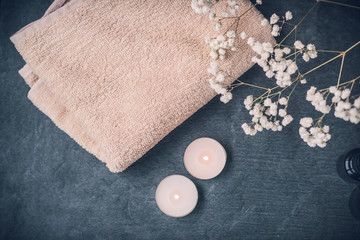 Light fluffy beige towels with spa paraphernalia, candles and flowers on a dark gray background