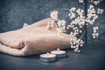 Light fluffy beige towels with spa paraphernalia, candles and flowers on a dark gray background