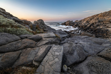 Amazing view of the sunset over the water in the Chilean coast. An idyllic scenery with the sunlight illuminating the stone pavement with orange tones and the sea in the background under a moody sky
