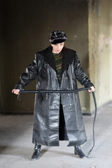 A domineering lady in a black leather cloak with a whip in her hand. The concept of BDSM