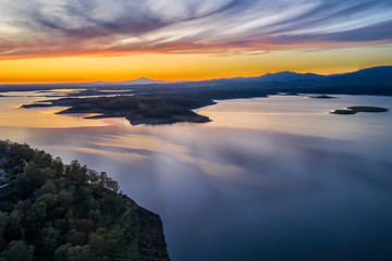 Aerial view of Gabriel y Galan lake at Extremadura countryside. An amazing view during sunset time on a cloudy day. The colors of the sky reflected over the lake waters give an idyllic landscape view
