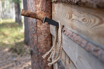 A knife with a wooden handle is stuck in a wooden board. A twisted rope hangs on a knife.