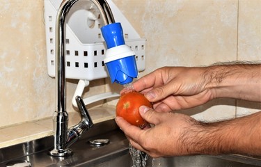 Lavando  un tomate bajo un torrente de agua, que brota de un grifo azul, de un lava loza de una...