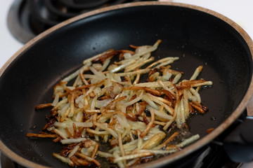 Fresh shredded, hashbrown potatoes frying in a pan with oil on the stove.