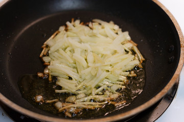 Fresh shredded, hashbrown potatoes frying in a pan with oil on the stove.