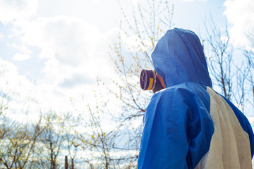 man in protective overalls and mask stands with his back on the background against the sky and trees