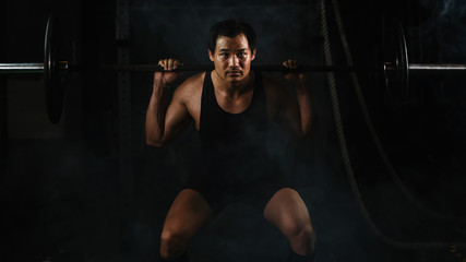 Fototapeta na wymiar asian athletic strong man having workout and bodybuilding with barbells weightlifting backsquat style in gym and fitness center in dark tone
