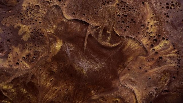 Colorful gold dust and brown paint like chocolate flows mixing in fantastic design and patterns. Golden sparkling particles, ink drops and mixing. Multicolored liquid background in motion