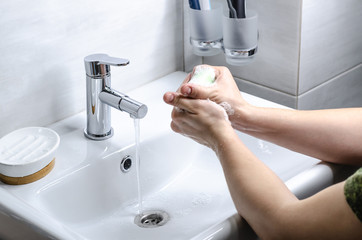 Hand washing with soap. Preventive measures against infection. A young guy washes his hands with soap in the bathroom. Body hygiene. The fight against COVID-19.