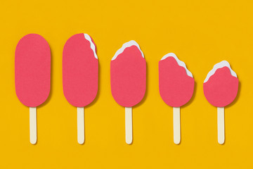 Paper ice-cream on yellow background in different stages of eating. Minimalist concept.  Set of five strawberry ice cream on wooden stick. Paper craft.