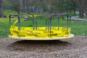 A merry-go-round is wrapped in yellow caution tape warning children and their parents not to use the playground equipment during the COVID-19 or coronavirus epidemic.