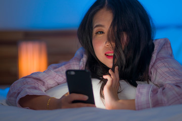 Obraz na płótnie Canvas young beautiful and happy sweet Asian Chinese woman and pajamas enjoying online with hand phone in bed at night playing social media at home in internet addiction