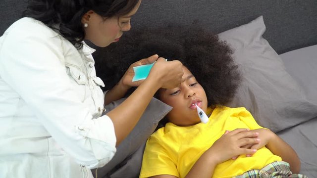 4K African American mother using hand and digital oral thermometer checking temperature of illness with cold and flu daughter child girl and put fever patch on her head. Children healthcare concept.