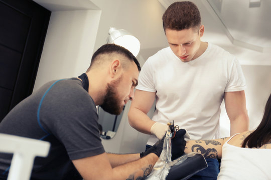 Professional tattoo master teaching young specialist in salon. Internship concept